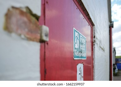 Milton Keynes, UK - Circa March 2020: Shallow Focus Of An Old Fire Exit And No Smoking Sign Seen Attached For A Fire Door, Used For Emergency Exit For A Warehouse And Logistics Company.