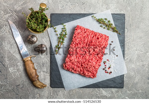 Minced meat on paper and slate with\
seasoning and fresh thyme on gray background, top\
view