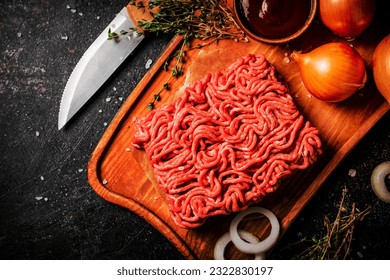 Minced meat on a wooden cutting board with onions and sprigs of thyme. On a black background. High quality photo - Powered by Shutterstock