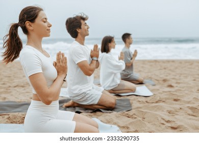 Mind harmony. Group of young yoga lovers meditating together during lesson outdoors on the beach, sitting in a row with clasped hands and closed eyes, free space - Powered by Shutterstock