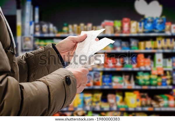 Minded man viewing receipts in supermarket and\
tracking prices