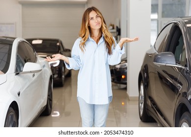 Minded Woman Customer Female Buyer Client Wears Blue Shirt Chooses Auto Between Two Cars Wants To Buy New Automobile In Car Showroom Vehicle Salon Dealership Store Motor Show Indoor. Sales Concept.