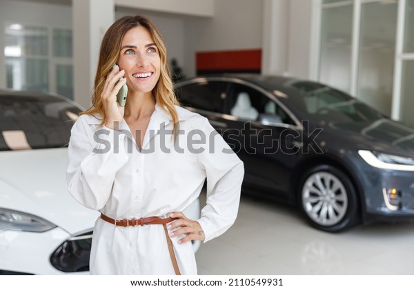 Minded woman customer female buyer client in\
white shirt talk on mobile cell phone choose auto want to buy new\
automobile in car showroom vehicle salon dealership store motor\
show indoor Sales\
concept