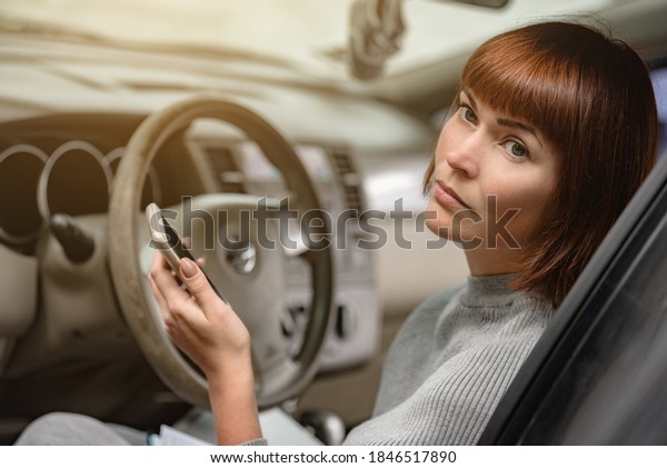 Minded woman driver\
sitting inside car and using delivery service on smartphone,\
part-time job in a free time in a taxi service, a girl in confusion\
the car broke down