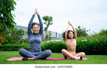 Mindful African Mom With Cute Funny Kid Daughter Doing Yoga Exercise At Park.calm Black Mother And Mixed Race Little Girl Doing Yoga In City Park Nature Together, Mum Teaching Child To Meditate.