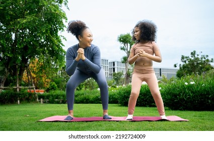 Mindful African Mom With Cute Funny Kid Daughter Doing Yoga Exercise At Park.calm Black Mother And Mixed Race Little Girl Doing Yoga In City Park Nature Together, Mum Teaching Child To Meditate.