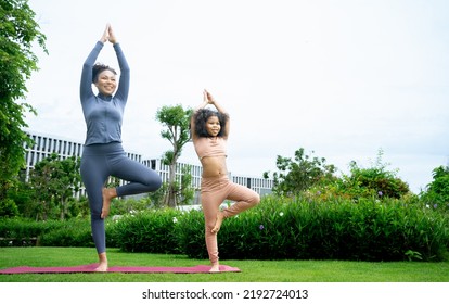 Mindful African Mom With Cute Funny Kid Daughter Doing Yoga Exercise At Park.calm Black Mother And Mixed Race Little Girl Doing Yoga In City Park Nature Together, Mum Teaching Child To Meditate.