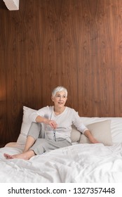 Mindful Beautiful Senior Woman With Glasses Sitting On A Comfy Bed And Getting Ready For Sleep In Her Bright Modern Bedroom, Night Routine And Bedtime Concept