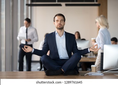 Mindful Calm Businessman In Suit Meditating At Office Sitting In Lotus Position On Work Desk, Successful Ceo Executive Doing Yoga Exercise At Workplace, Peace Of Mind, No Stress Free Relief Concept