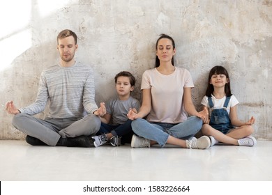 Mindful Calm Happy Fit Family Of Young Parents And Little Kids Sitting Together On Heated Warm Wooden Floor In Lotus Positions, Meditation, Practicing Breathing Yoga Exercises. Wellness Hobby Concept