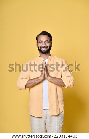 Mindful happy bearded indian man praying in meditation holding hands in namaste, feeling mental balance, stress free, meditating in prayer, doing yoga isolated on yellow background. Vertical.