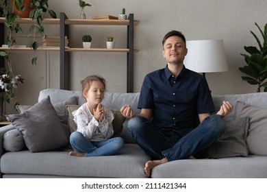Mindful happy relaxed two generations family sitting in lotus position on couch, meditating doing yoga breathing exercises, enjoying peaceful time together in modern living room, hobby activity.