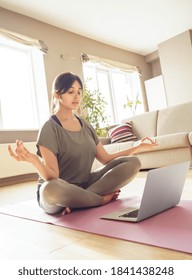 Mindful Indian Woman Meditating Watching Live Online Tv Pilates Class Tutorial Using Laptop Computer At Home Doing Yoga Virtual Training Fitness Workout Meditation Exercise In Apartment, Vertical.