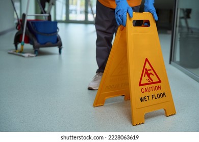 Mindful janitor putting plastic caution sign on the wet floor