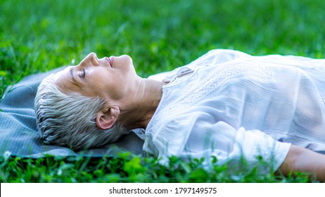 Mindful Mature Woman Meditating By The Water, Lying Down, Feeling Connected To The Earth And Nature