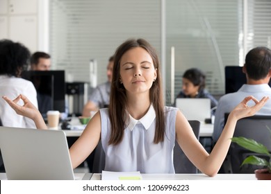 Mindful millennial girl meditating in office taking break for meditation at work, young woman managing stress practicing yoga at workplace for mental emotional balance, no stress free relief concept