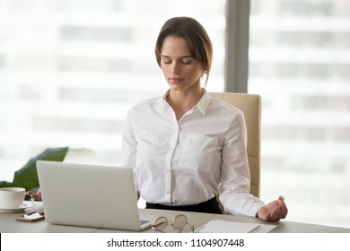 Mindful millennial woman taking break for relaxation meditating in office to reduce work tension, calm successful businesswoman doing yoga exercises feeling zen enjoying no stress free relief concept