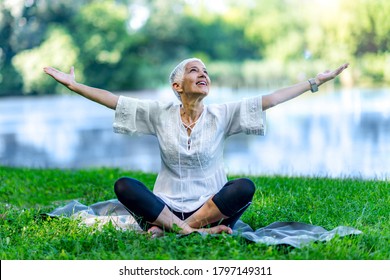 Mindful senior woman, feeling overwhelmed by beauty of the, meditating, sitting by the water with open arms