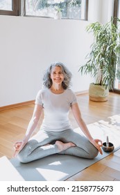 Mindful Senior Woman Sitting Cross-legged At The Yoga Mat, Practicing Yoga And Enjoying Meditation. Mature Lady With Crossed Legs Meditating At Home