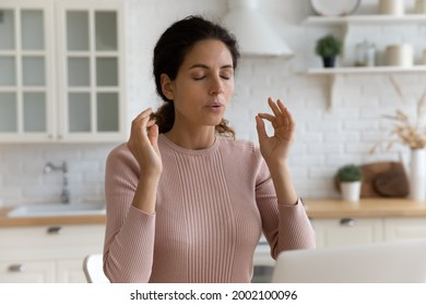 Mindful young woman breathing out with closed eyes, calming down in stressful situation, working on computer in modern kitchen. Millennial hispanic lady managing stress, practice yoga at home office. - Shutterstock ID 2002100096
