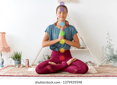 mindfulness, spirituality and healthy lifestyle concept - woman meditating in lotus pose at yoga studio with seven chakra symbols