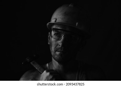 Miner, Dirty In Coal Soot, Wearing Helmet, Protective Glasses And With Hammer In His Hands In Black And White Photo