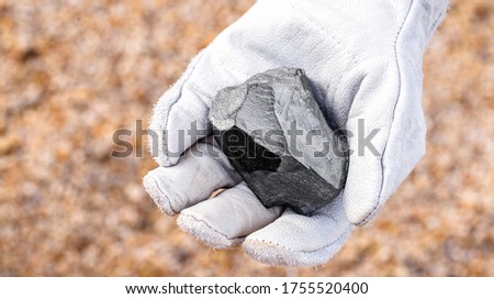 miner hand holding iron stone, metallic iron pyrite, steel, used in heavy industrial production. Mineral extraction concept.