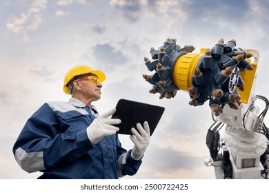 Miner operator in helmet with tablet computer control drilling machine in coal mine. Concept smart industrial mining