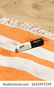 Mineral SPF50 protector solar stick con protección UVA + UVB en la toalla de playa naranja en la arena cerca del mar, rutina Beaty para una piel sana contra el daño solar. Vertical