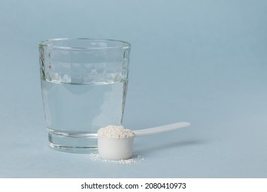 Mineral supplement diatomaceous earth or diatomite powder in a plastic spoon. White powder in a scoop and glass of water for preparation of the detox drink