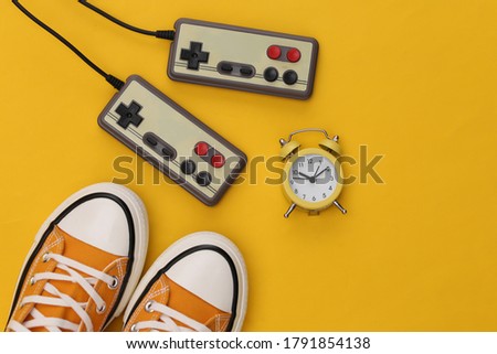 Mini alarm clock and retro joysticks, sneakers on yellow background. Time to play video games. 80s. Top view