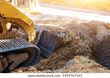 Mini bulldozer working with earth while doing landscaping works on construction moving soil