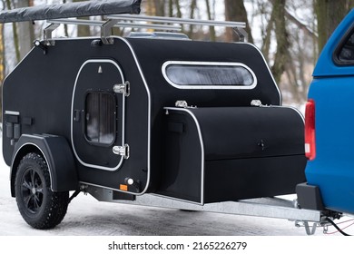 Mini Camper Towed By A Blue Muscle Car In The Winter Snow Woods. Family Journey Time Together Away In The Forest Wild Life. Pick Up Truck With RV Travel Trailer Driving Though National Park.