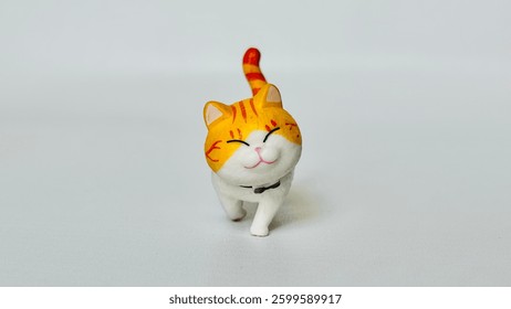 Mini cat doll made of plastic. With a happy smiling face. Walking on the white floor. Orange cat. Free space for text.