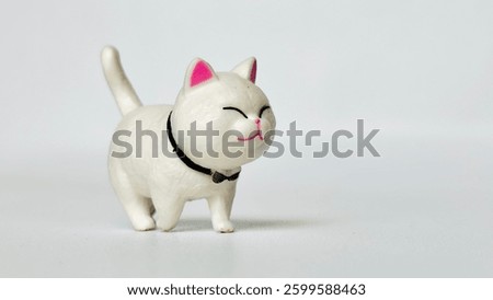 Mini cat doll made of plastic. With a happy smiling face. Walking on the white floor. White cat. Free space for text.