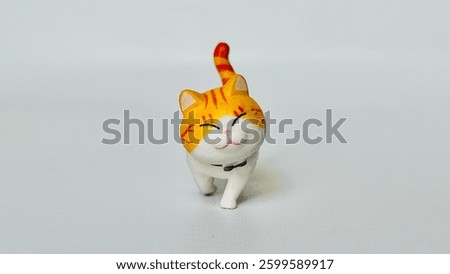 Mini cat doll made of plastic. With a happy smiling face. Walking on the white floor. Orange cat. Free space for text.