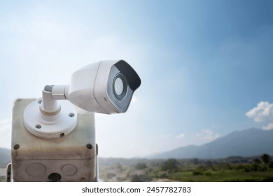 mini cctv camera installed on metal post above rice paddy field, guest houses and mountain background, concept for using mini ip cctv camera to monitor or to do the security.