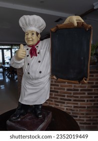 A mini chef statue holding an empty menu blackboard in a restaurant