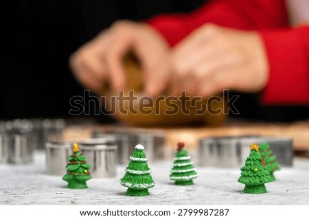 Mini Christmas tree decorations with cookie cutters in foreground and gingerbread dough preparation in background. Festive holiday baking concept featuring homemade treats, seasonal traditions and winter celebrations