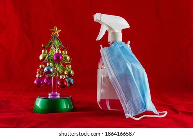 Mini Christmas Tree Next To An Antiseptic Spray Wearing A Blue Facemask. Christmas In The Covod-19 Era Concept Photo.