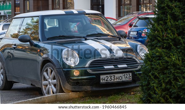 Mini Cooper\
car is parked in parking lot in city landscape park. City in south\
of Russia. Close-up. Car is dark blue with white stripes on hood.\
Krasnodar, Russia - 05 November\
2020