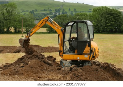 Mini digger moving earth in a field in rural countryside.