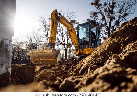 Mini excavator digging a trench next to a building