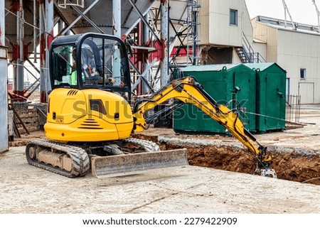 mini excavator digs a trench at a construction site. Laying of underground sewer pipes and communications during construction. Compact construction equipment. Earthworks, excavation