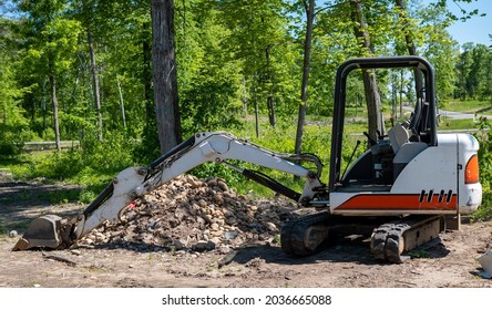 A Mini Excavator On Dirt Near A Pile Of Rocks At A New Home Construction Lot.