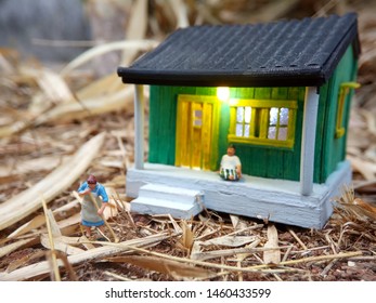 Mini Figure Toy Indonesian Woman Cleaning The Terrace And Old Man Using Sarung, Kopiah And White Shirt, Sit At His House, Beyond Bamboo Forest With Copy Or Negative Space For Text Placement Area