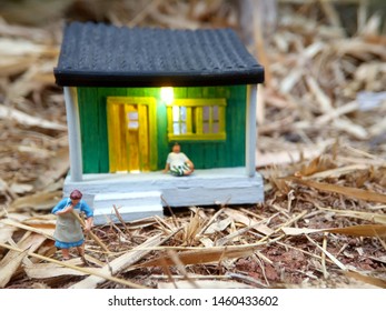 Mini Figure Toy Indonesian Woman Cleaning The Terrace And Old Man Using Sarung, Kopiah And White Shirt, Sit At His House, Beyond Bamboo Forest With Copy Or Negative Space For Text Placement Area