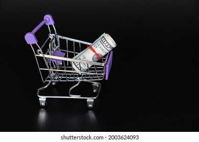 Mini Food Basket With 100 Dollars On A Black Background. Investing And Storing Money. The Concept Of Frugality And Financial Literacy.