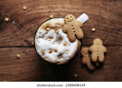 Mini gingerbread men on the edge of a festive coffee cup with frothy milk and little golden sugar stars. All on a dark wooden background.  - Powered by Shutterstock