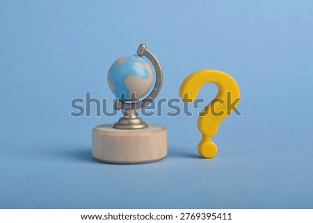 Mini globe with question mark on blue background, symbolizing global uncertainty, geography questions, travel decisions, and worldwide concept.